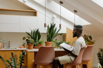 a man reading a book on a table surrounded with snake plant and other house plants